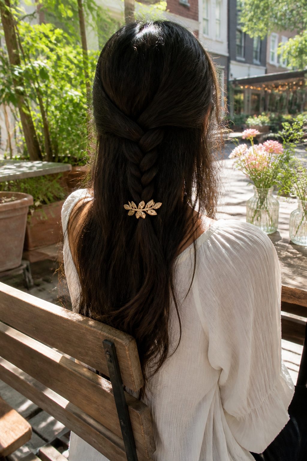 Half-back braid held at the end by a decorative barrette in an outdoor cafe.